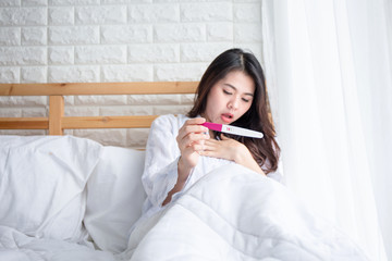 Selective focus Pregnancy test positive result on hand of  woman ,have morning sickness  pregnant woman on bed in her bedroom .