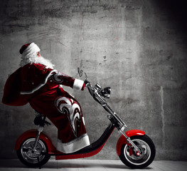 Fototapeta na wymiar Santa Claus ride motorcycle bicycle scooter with bag full of present gifts with text copy space. New year and Merry Christmas