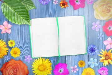 Beautiful flower frame with notebook in center on purple wooden planks background. Floral composition of spring or summer flowers.