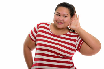 Studio shot of young happy fat Asian woman smiling and listening
