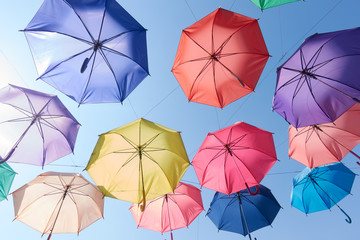 colorful umbrellas hang on to bright blue sky background