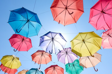 colorful umbrellas hang on to bright blue sky background