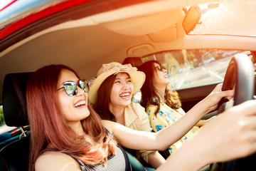 Enjoying woman with her girlfriend   in red car summer vacation, holidays, travel, road trip and people concept .