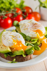 Avocado toast, cherry tomato and poached eggs on wooden background. Breakfast with vegetarian food, healthy diet concept.