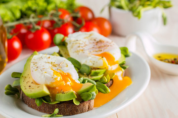 Avocado toast, cherry tomato and poached eggs on wooden background. Breakfast with vegetarian food, healthy diet concept.