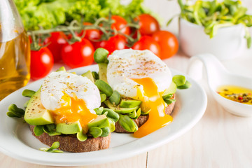 Avocado toast, cherry tomato and poached eggs on wooden background. Breakfast with vegetarian food, healthy diet concept.