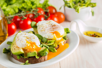 Avocado toast, cherry tomato and poached eggs on wooden background. Breakfast with vegetarian food, healthy diet concept.