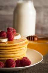 Tasty pancakes with blackberries, banana, raspberries, eggs, honey and maple syrup on wooden background. Morning breakfast concept.