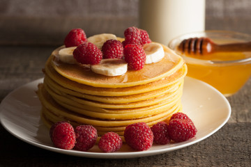 Tasty pancakes with blackberries, banana, raspberries, eggs, honey and maple syrup on wooden background. Morning breakfast concept.