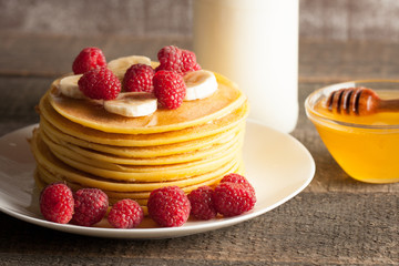 Tasty pancakes with blackberries, banana, raspberries, eggs, honey and maple syrup on wooden background. Morning breakfast concept.