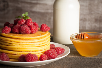 Tasty pancakes with blackberries, banana, raspberries, eggs, honey and maple syrup on wooden background. Morning breakfast concept.