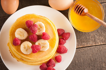 Tasty pancakes with blackberries, banana, raspberries, eggs, honey and maple syrup on wooden background. Morning breakfast concept.