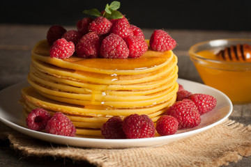 Tasty pancakes with blackberries, banana, raspberries, eggs, honey and maple syrup on wooden background. Morning breakfast concept.