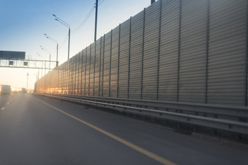 Fototapeta na wymiar Morning traffic on a highway with lighting poles and metal rails of the safety barrier