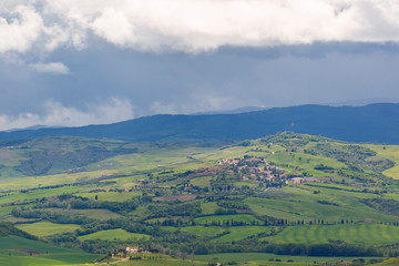 View of a valley in Tuscany with a village and rain clouds in the sky