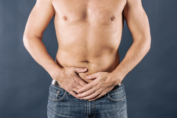 Obraz premium Man holding his urethra in pain. Man with naked torso experience urethra pain on blue background. Medical concept
