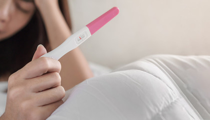 Unhappy young asian woman holding pregnancy test showing a negative result, Selective focus and copy space, Wellness and healthy concept, Infertility problem.