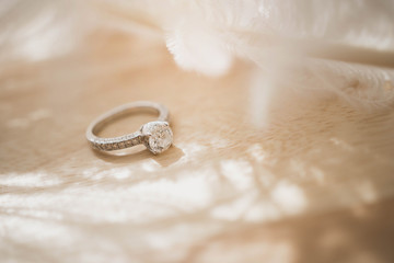 Close up of an elegant diamond ring and feather on wood background. soft and selective focus. Love and wedding concept. - obrazy, fototapety, plakaty