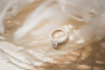 Close up of an elegant diamond ring and feather on wood background. soft and selective focus. Love and wedding concept.