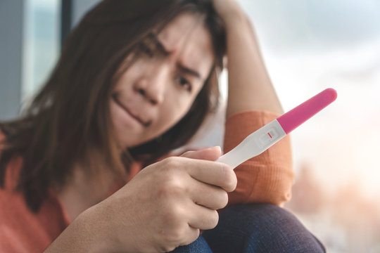 Unhappy young asian woman holding pregnancy test showing a negative result and sit down near big window city view , Wellness and healthy concept, Infertility problem, Selective focus.