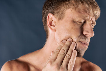 Naklejka premium Sad depressed man in pain holding his cheek. Portrait of a man on blue background. emotion facial expression. feelings and people reaction. Toothache