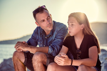 Father and daughter sitting on a rocky beach and talking