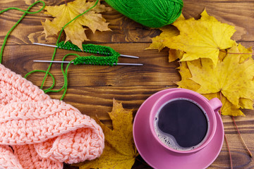 Cup of coffee, ball of yarn, knitting, knitted scarf and yellow maple leaves on wooden table. Autumn still life