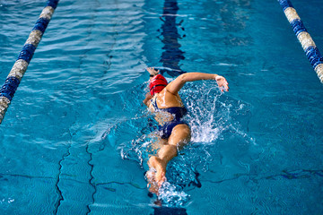Female athlete swimming fast in crawl style.  Splashes of water scatter in different directions.