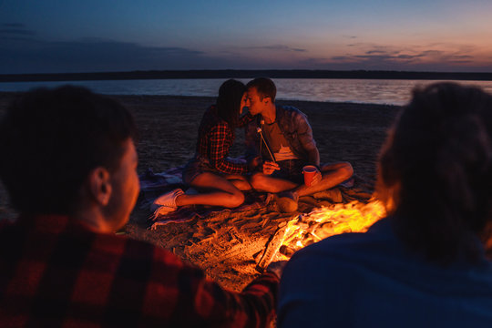 Camp on the beach. Group of young couples having picnic with bonfire. One couple is kissing