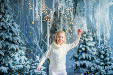 Christmas portrait of happy blonde child girl indoor studio, snowy winter decorated tree on background. New Year Holidays