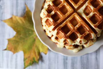 Belgian waffles and autumn maple leaf on light wooden table. Freshly cooked homemade dessert, remedy for autumn depression