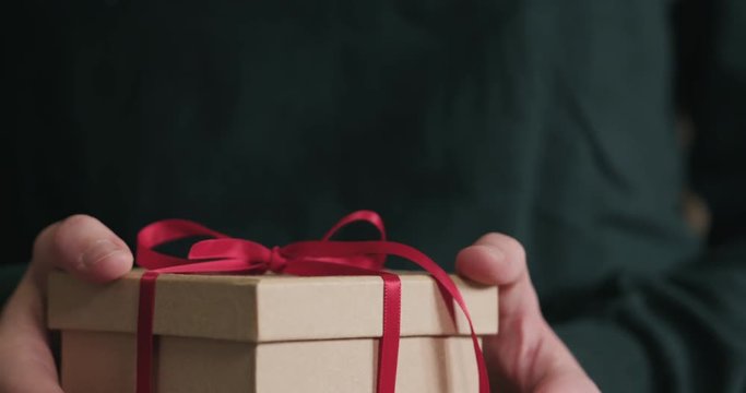 Slow motion closeup female hands holds paper gift box with red ribbon bow
