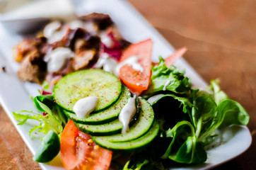tasty dish with pork, lettuce, tomato and cucumber on a white plate with a dip