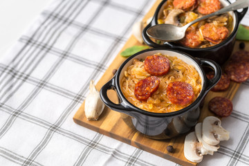 Slovak Christmas national cabbage soup in two small black pots with sausage on the tablecloth background.