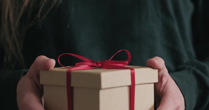 Slow motion closeup female hands holds paper gift box with red ribbon bow