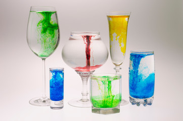 Still life with glasses of different heights filled with the effect of water smoke with a multi-colored food coloring on a white background.