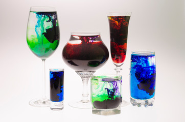 Still life with glasses of different heights filled with the effect of water smoke with a multi-colored food coloring and ink on a white background.