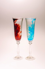 The effect of water smoke using an red and blue food coloring in two glasses for champagne on a white background.