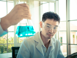 hand of the scientist  show the Erlenmeyer flask the othe asian scientist looking to the erlenmeyer...