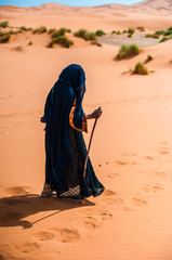 old  berber woman walking alone on a sand dune in Merzouga, Morocco