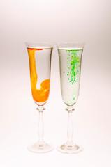 The effect of water smoke using an orange and green food coloring in two glasses for champagne on a white background.