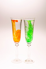 The effect of water smoke using an orange and green food coloring in two glasses for champagne on a white background.