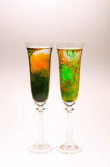 The effect of water smoke using an orange and green food coloring in two glasses for champagne on a white background.