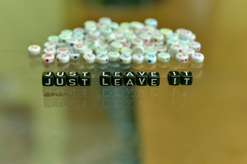 JUST LEAVE IT  written with Acrylic Black cube with white Alphabet Beads on the Glass Background