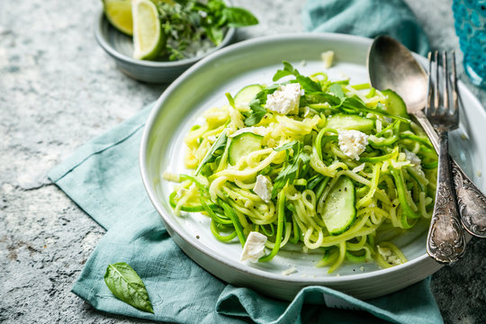 Zucchini noodles with cucumber, feta cheese and arugula, rustic background