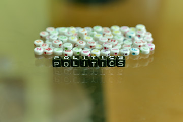 POLITICS  written with Acrylic Black cube with white Alphabet Beads on the Glass Background