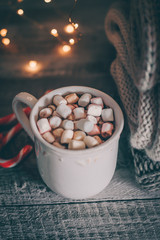 Obraz na płótnie Canvas Stack of cozy knitted sweaters and cup of coffee or hot chocolate with marshmallow on wooden background. Autumn-winter concept. Magic, cozy and mood time