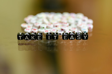 TAKE IT EASY written with Acrylic Black cube with white Alphabet Beads on the Glass Background