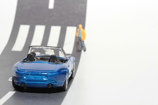 automobile e uomo anziano in miniatura che attraversa la strada sulle strisce pedonali