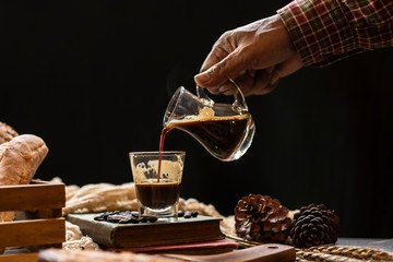 hand holding cup of coffee and pouring to clear glass in coffee shop.
